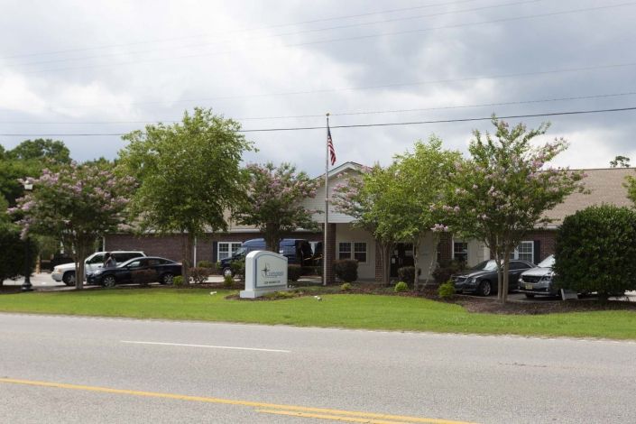 A building surrounded by trees and parked cars along a street under a cloudy sky.