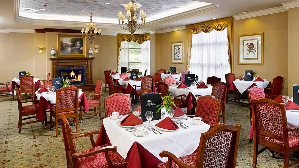 An elegant dining room with neatly arranged tables and chairs, featuring rich decor and a cozy fireplace.
