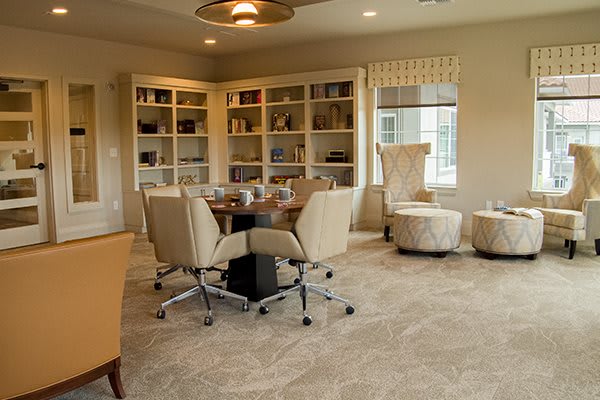 A modern conference room featuring a round table surrounded by comfortable chairs, with bookshelves lining the walls.