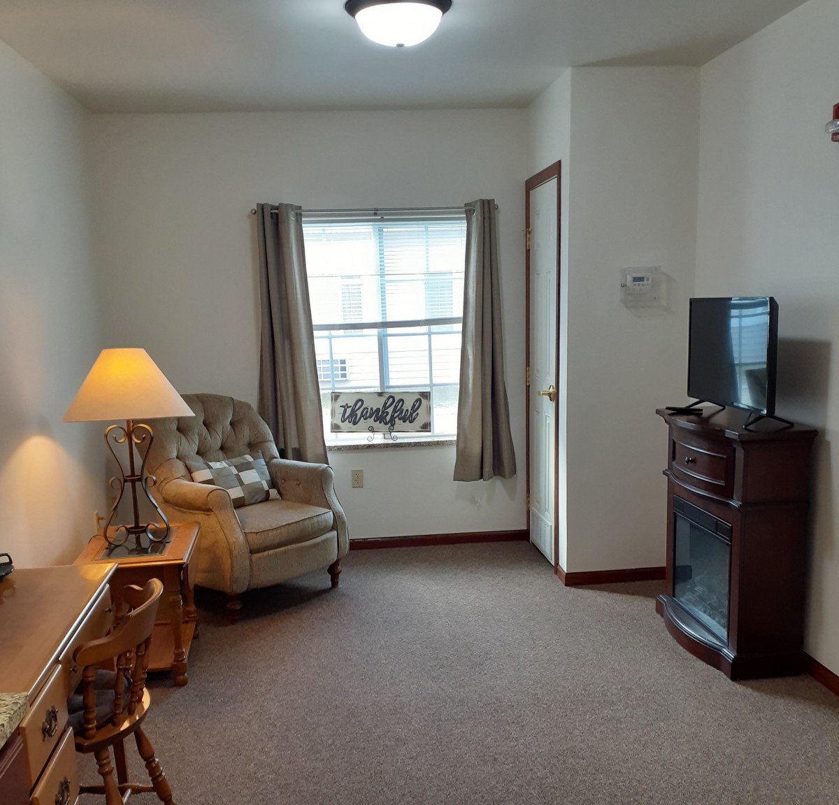 A cozy living room with a chair, desk, lamp, and television.