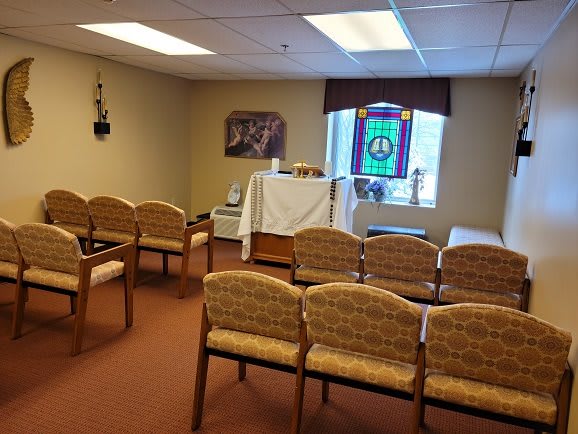 A small chapel with chairs arranged in rows facing an altar, featuring a stained glass window.