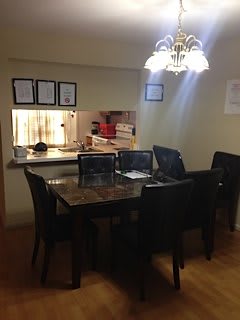 A cozy dining area with a marble table and black chairs, illuminated by a pendant light, adjacent to a kitchen pass-through.