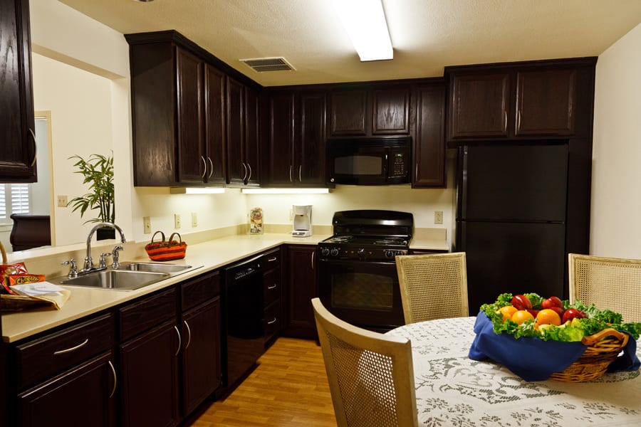 A cozy kitchen with dark cabinets and modern appliances, featuring a dining table adorned with a fruit bowl.