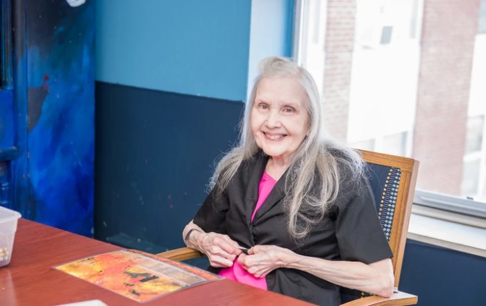 An elderly woman smiling while seated indoors.
