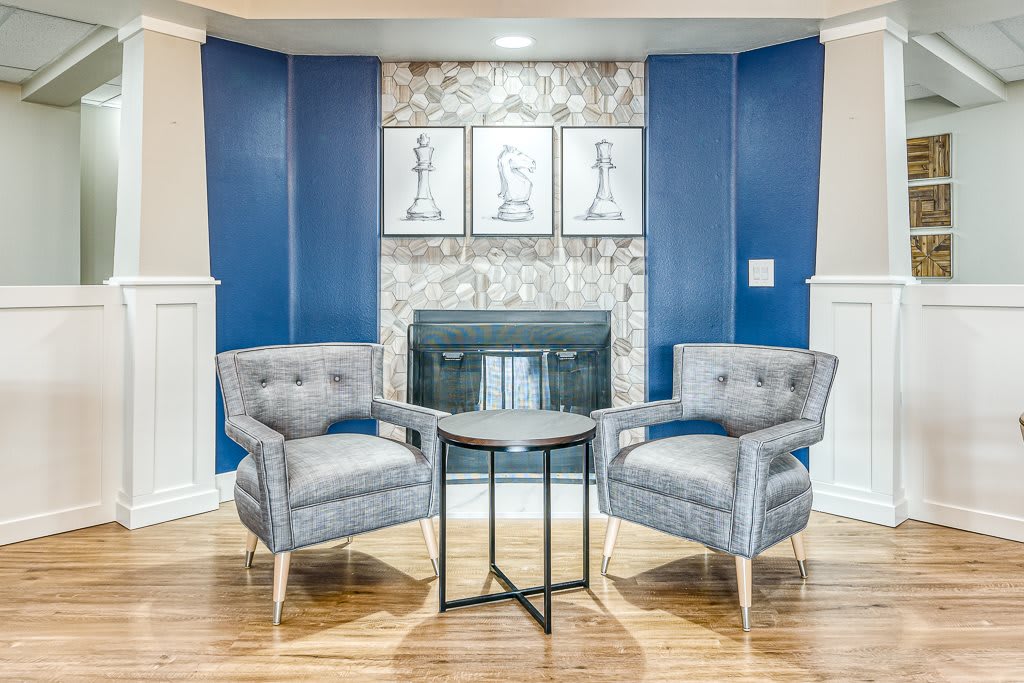 A stylish living room setup featuring two gray chairs facing each other with a small table in between, set against a blue accent wall and a fireplace, complemented by framed artwork.