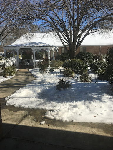 A serene winter scene featuring a garden with snow, a gazebo, and bare trees.