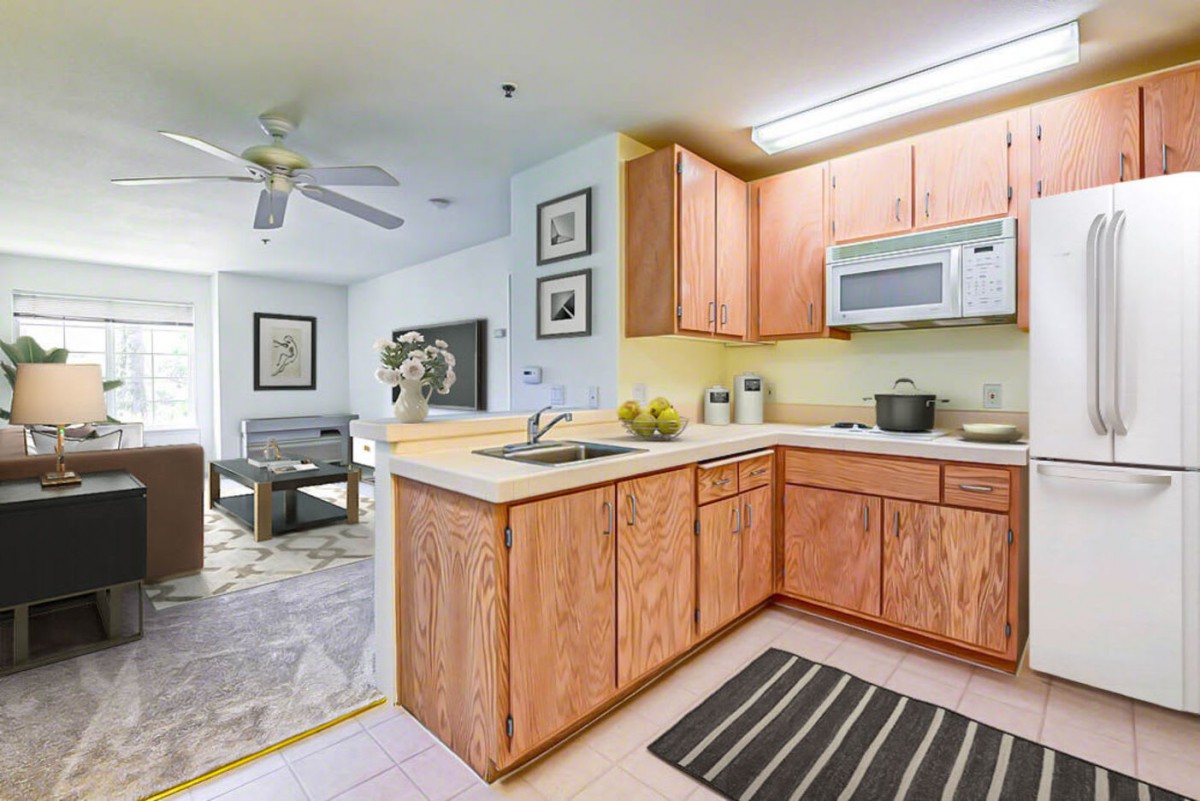 A modern open-concept kitchen with wooden cabinets, adjacent to a cozy living area.