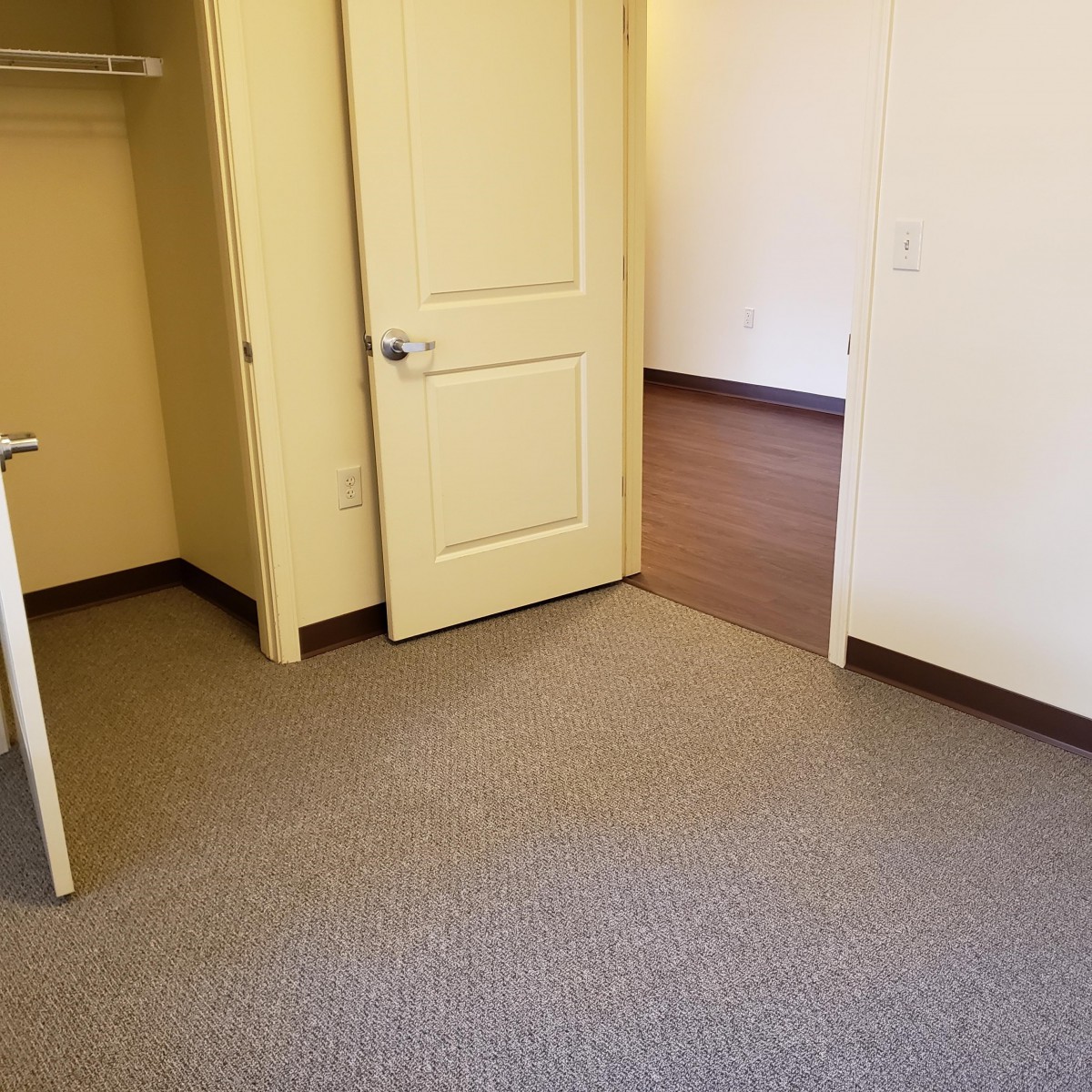 An empty room with a carpet, open door, and closet.