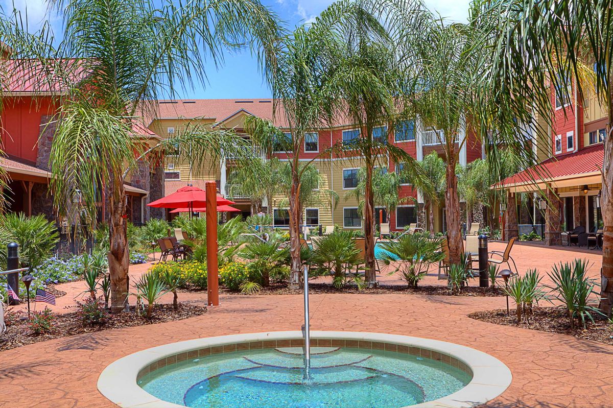A serene outdoor garden area with a small fountain surrounded by palm trees and hotel buildings.
