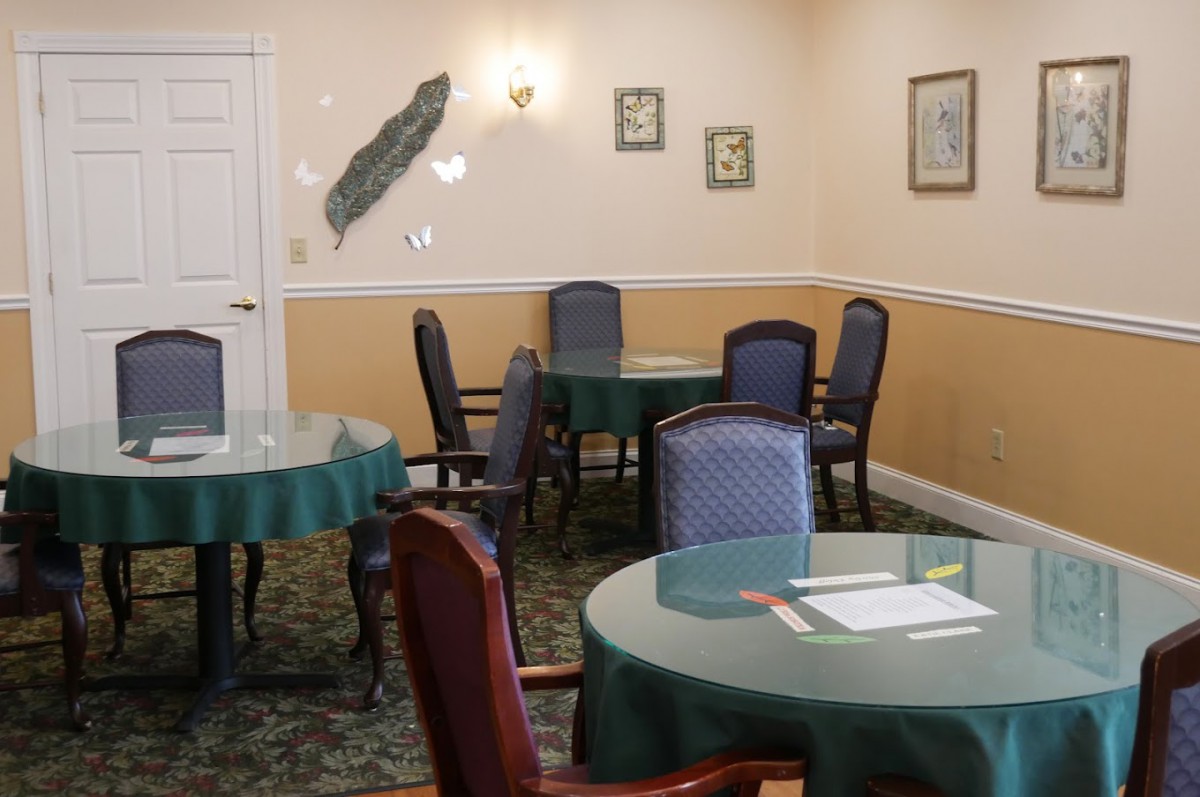 A cozy dining room with round tables covered in green tablecloths and surrounded by comfortable chairs.
