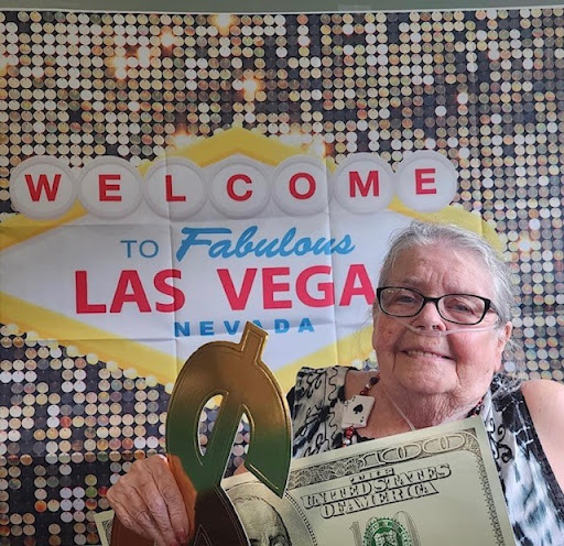 An elderly woman enjoying her visit to Las Vegas, holding a prop dollar bill in front of the iconic Welcome to Fabulous Las Vegas sign.