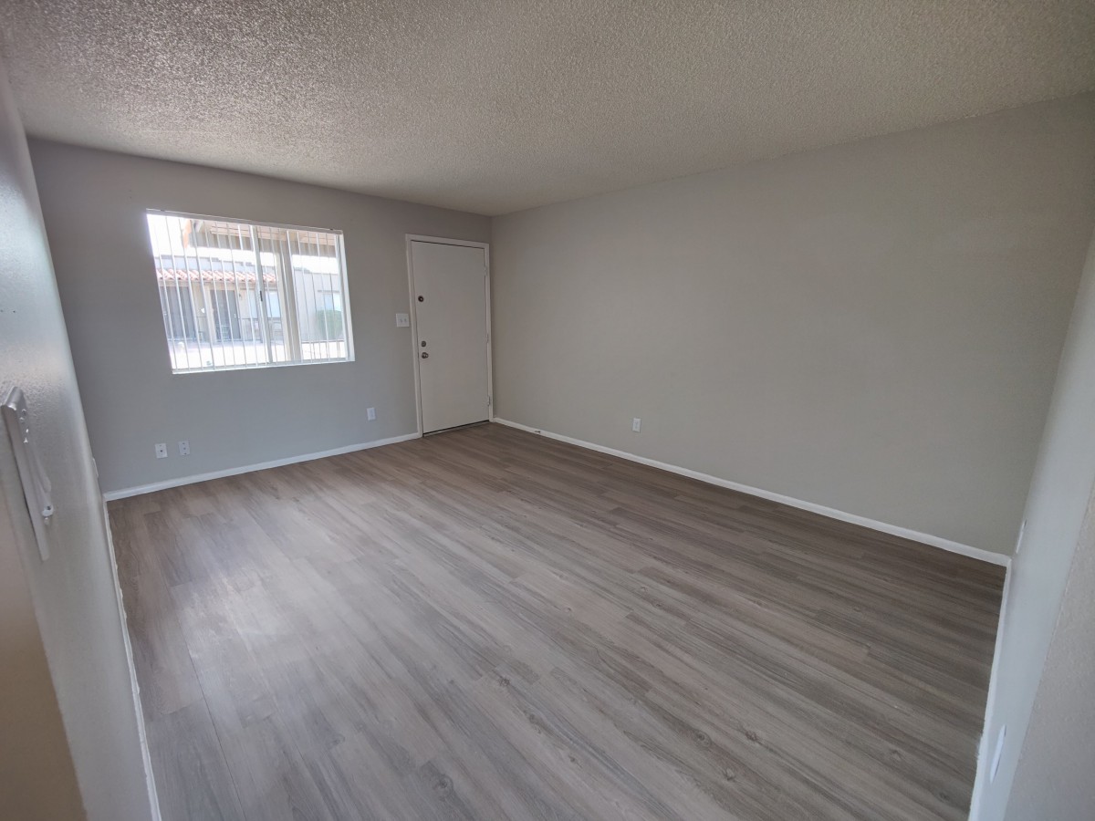 An empty room with hardwood flooring and natural light coming through a window.