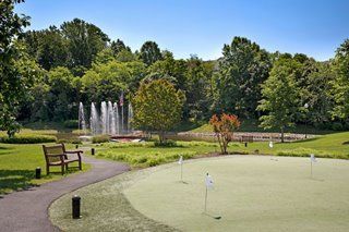 A scenic view of a golf course featuring a putting green and fountains amidst lush greenery.