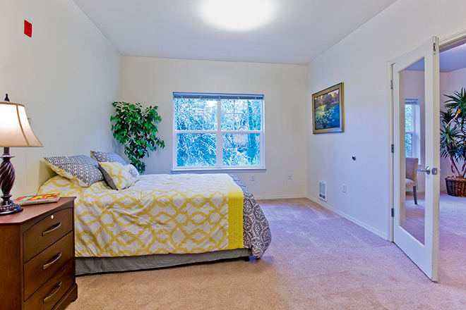 A bright and airy bedroom with a neatly made bed, large window, and tasteful decor.