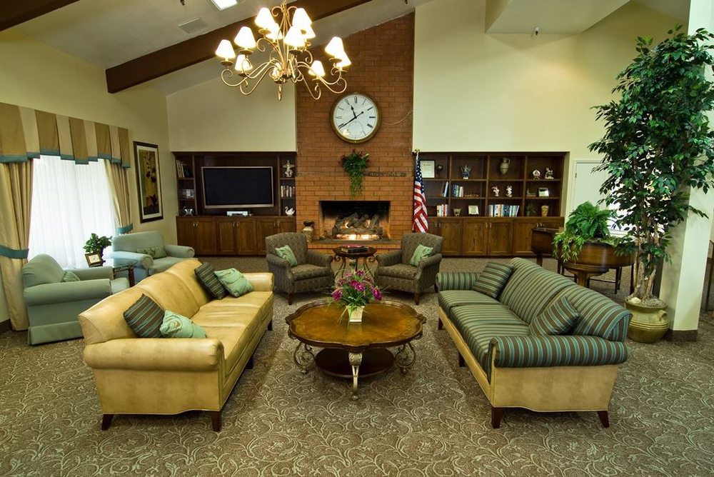 A cozy and well-decorated living room featuring sofas, a central coffee table, a fireplace with a clock above it, and built-in bookshelves.