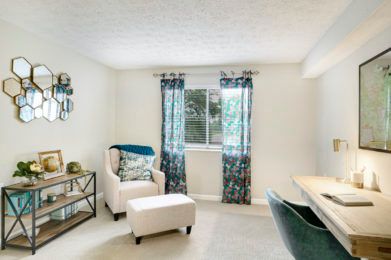 A cozy living room with an armchair and ottoman, featuring a bright window with patterned curtains.