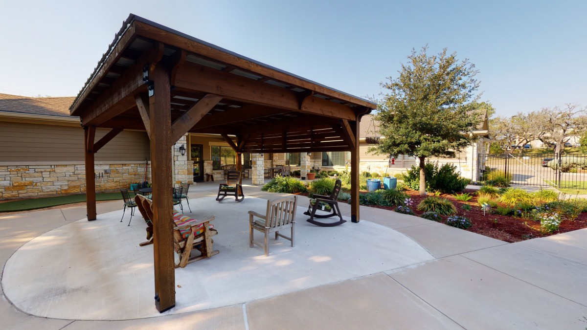 A wooden pergola with outdoor seating, surrounded by a landscaped garden.