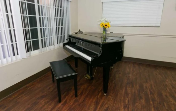 A grand piano with a bench and a vase of sunflowers on top, situated in a music room with hardwood floors.