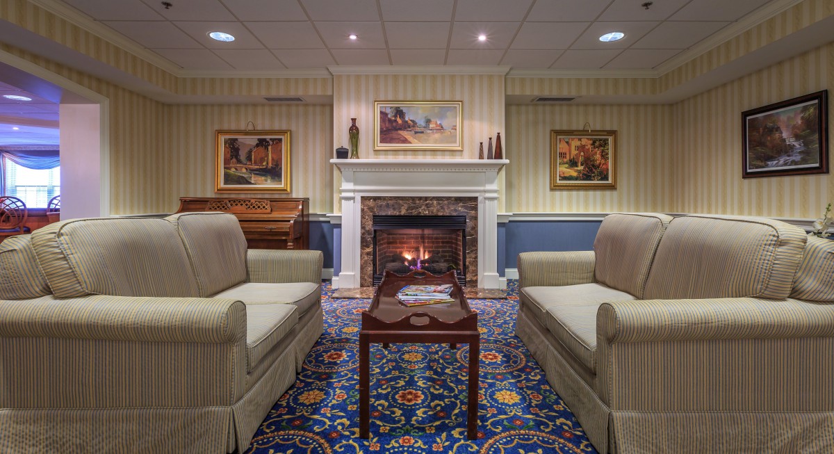 A cozy living room with a traditional fireplace, surrounded by sofas and decorated with artwork and a patterned carpet.