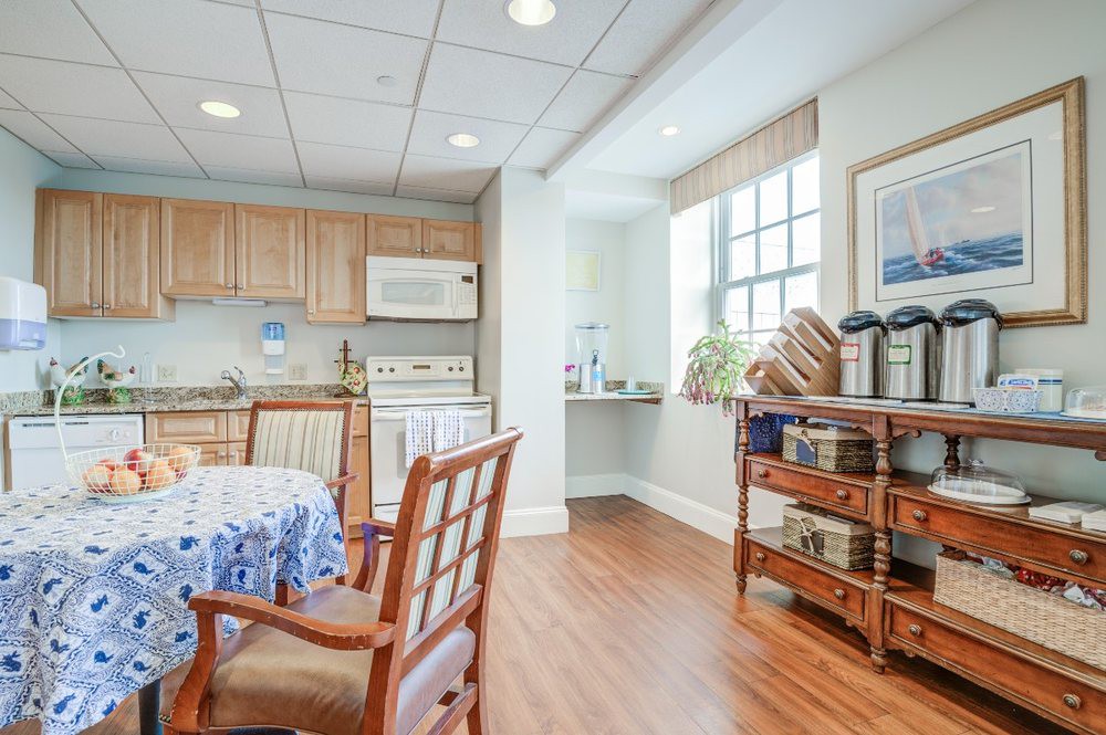 A cozy kitchen and dining area with wooden floors, featuring a table with chairs, ample natural light from the window, and a well-organized kitchen space.