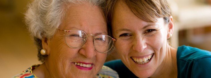 A close-up image of an elderly woman and a younger woman smiling together.