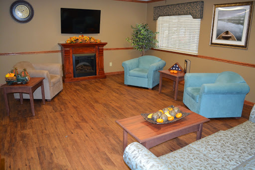A cozy living room featuring blue chairs, a wooden fireplace, and a TV mounted on the wall.