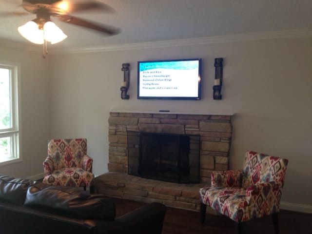 A cozy living room with a stone fireplace, wall-mounted TV, and patterned chairs.