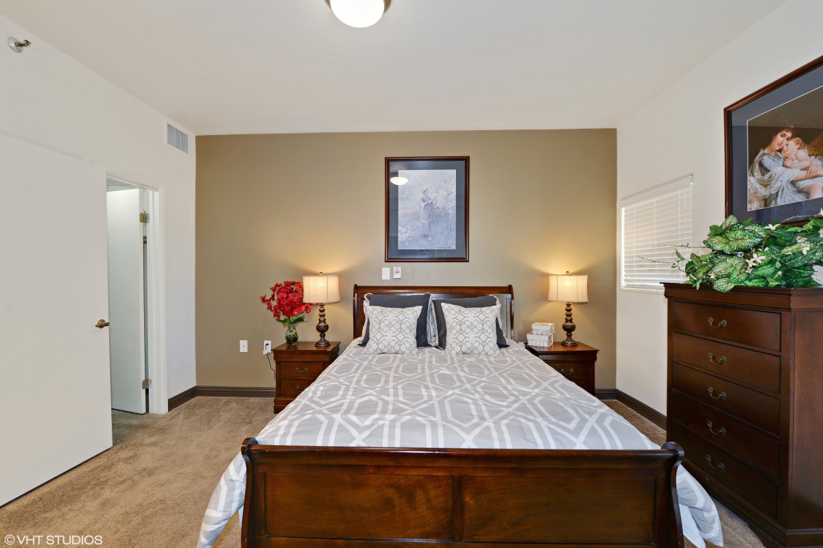 A well-decorated modern bedroom with a wooden bed and matching nightstands, featuring elegant lamps and wall art.
