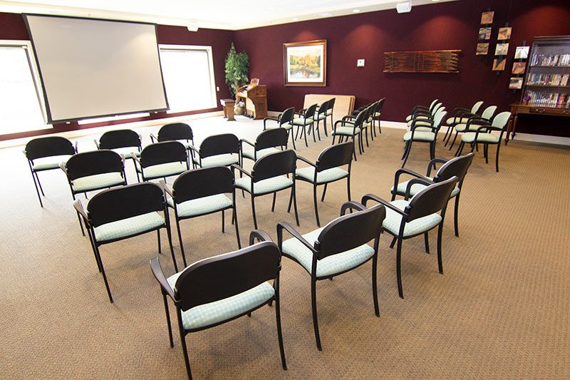 An empty conference room arranged with rows of chairs facing a projector screen.