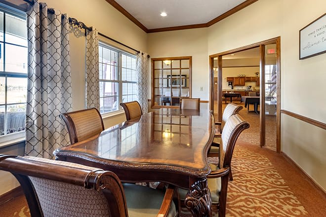 A well-furnished conference room with a large wooden table and comfortable chairs, illuminated by natural light through the windows.