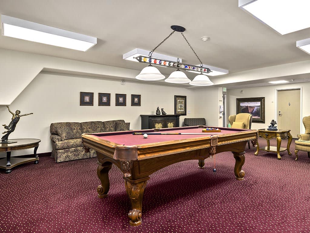 A cozy game room featuring a classic pool table with red felt, surrounded by comfortable seating and elegant lighting.