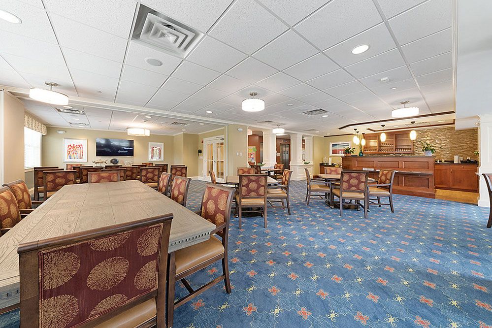 A well-lit dining area with tables and chairs, featuring elegant decor and patterned carpeting.