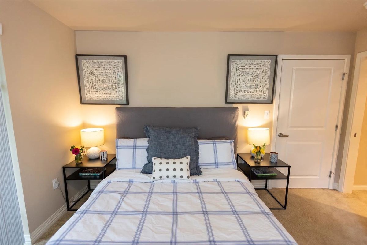 A neatly arranged bedroom featuring a bed with a checkered duvet, flanked by two nightstands and lamps.
