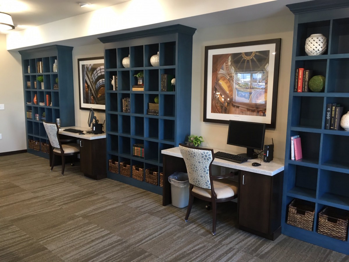 A modern office workspace featuring built-in shelves, two desks with computers, and elegant chairs.