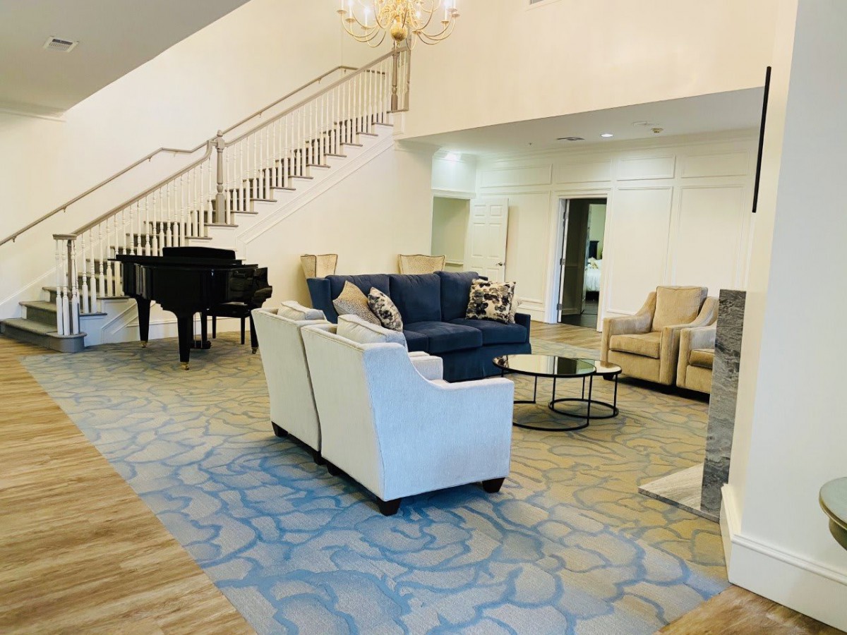 A spacious living room with elegant furniture and a grand piano near a staircase.