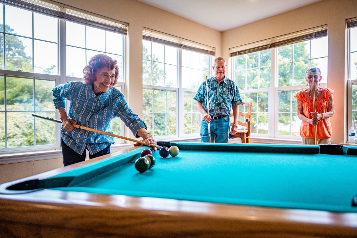 Two seniors enjoying a game of billiards in a sunlit room.