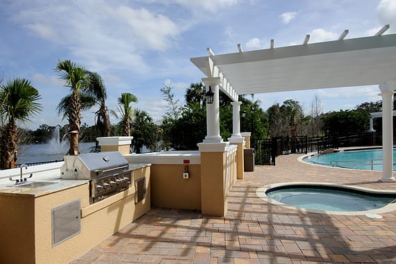 A beautiful outdoor patio area featuring a swimming pool, pergola, and grill under a clear sky.