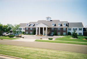 A large colonial-style building with manicured lawns in a suburban setting.