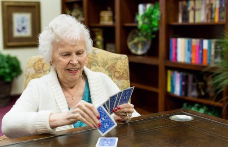 An elderly woman enjoying a game of cards in a library setting.