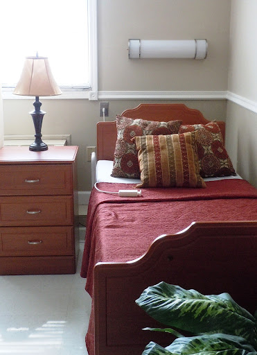 A cozy bedroom featuring a single bed with decorative pillows, a nightstand with a lamp, and a neatly arranged atmosphere.