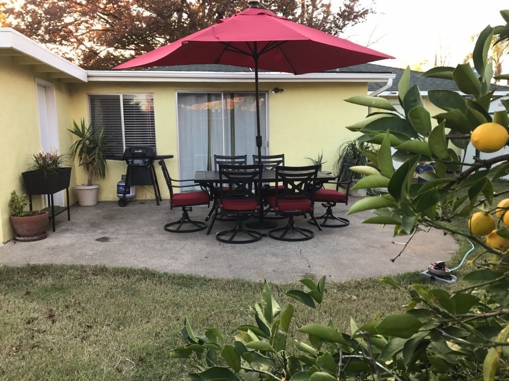 A cozy backyard patio with a red umbrella and outdoor dining set.