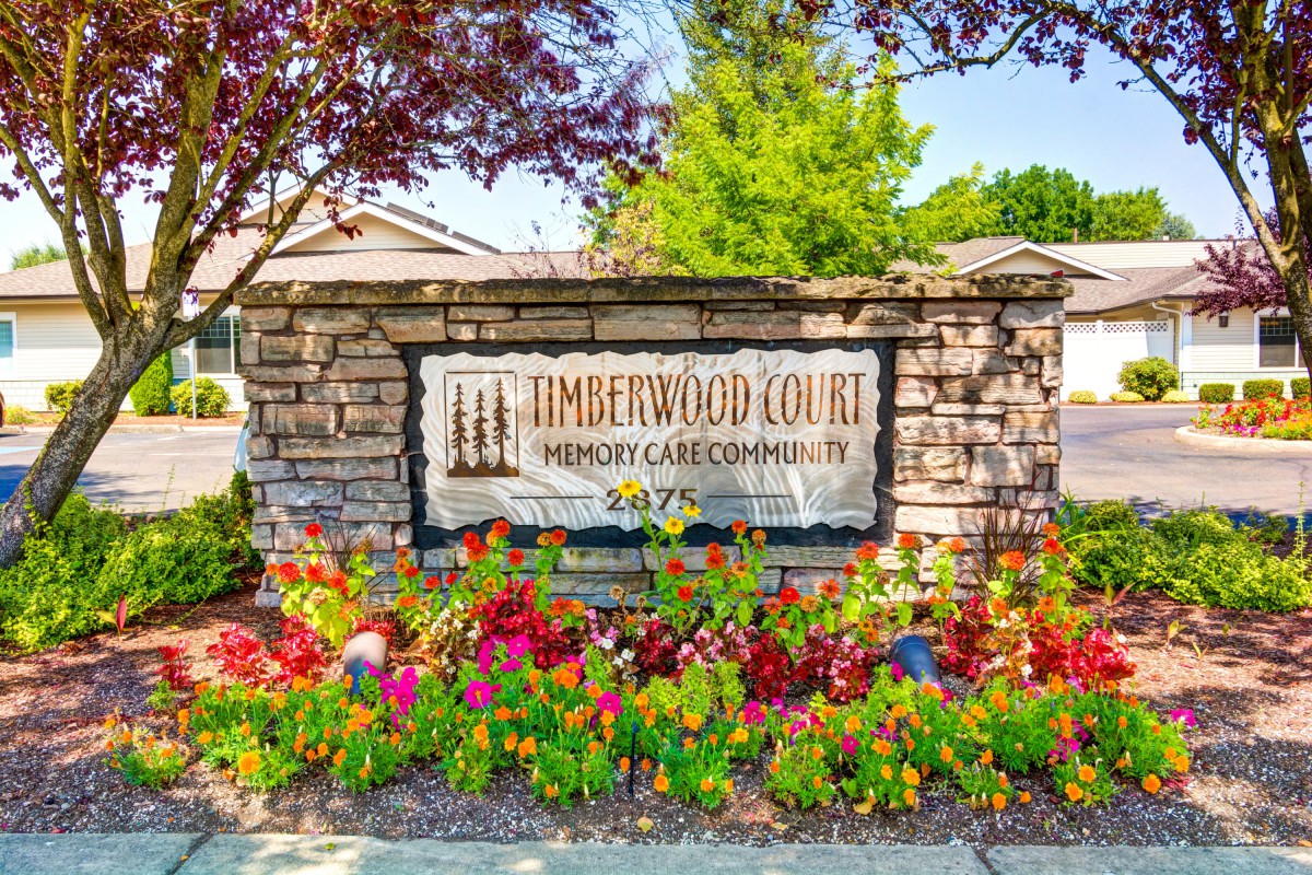 A stone sign surrounded by colorful flowers, marking the entrance to a memory care community.