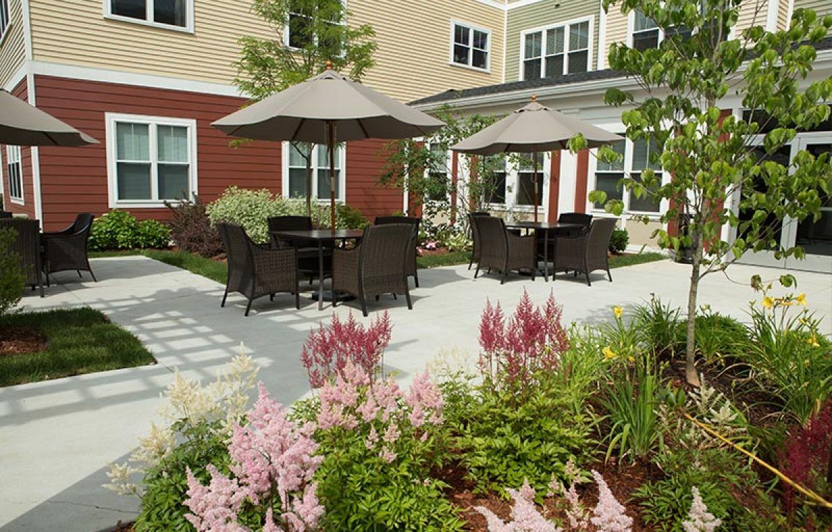 A beautifully landscaped garden patio with outdoor seating and umbrellas, adjacent to a residential building.
