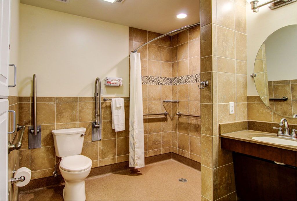An accessible bathroom featuring a walk-in shower with grab bars, a toilet, and neatly arranged towels.