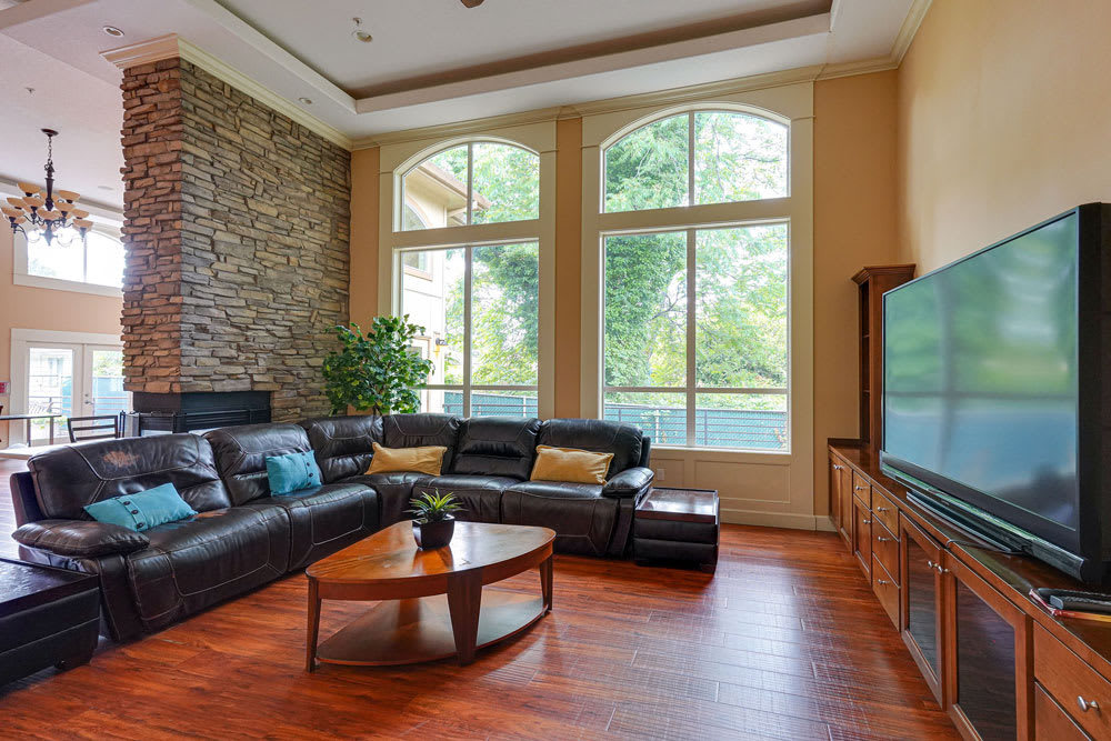 A modern living room with a leather sofa and large windows, featuring a stone accent wall and hardwood flooring.