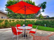 A cozy backyard patio setup with a red umbrella and matching chairs around a round table.