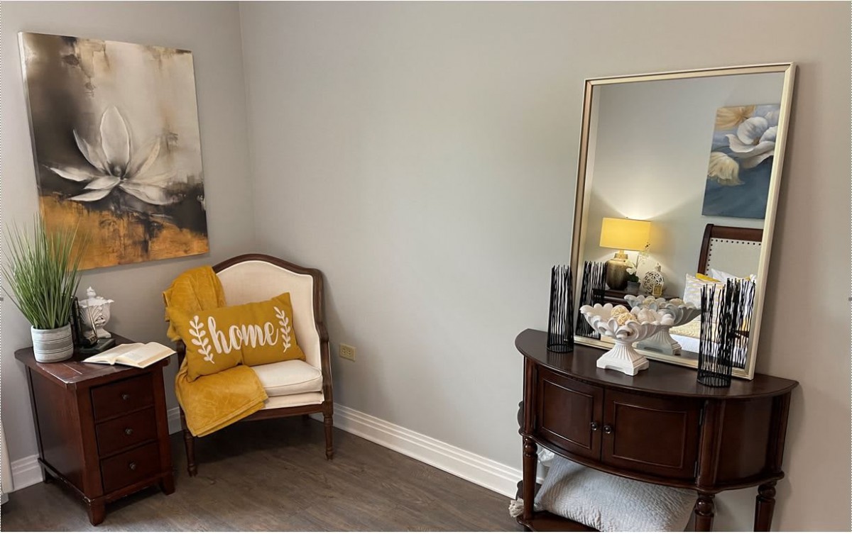 A cozy corner with an armchair, decorative pillow, and stylish side table featuring a lamp and mirror.