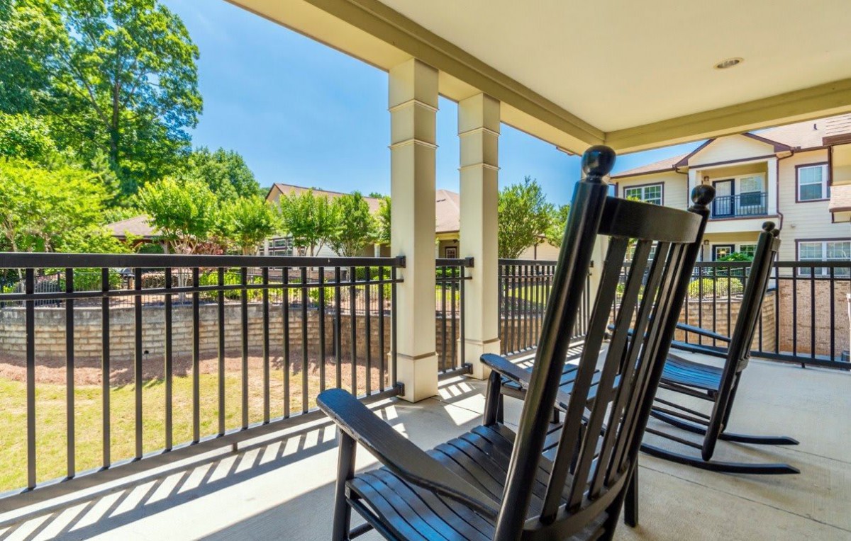 A sunny porch with black rocking chairs overlooking a peaceful outdoor area.