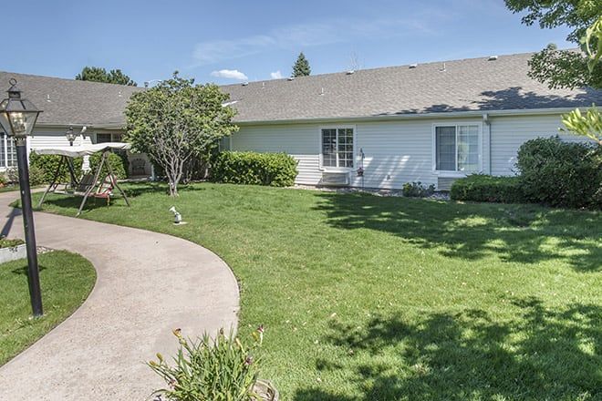 A backyard with a well-maintained lawn and garden, featuring a concrete pathway and surrounding greenery.
