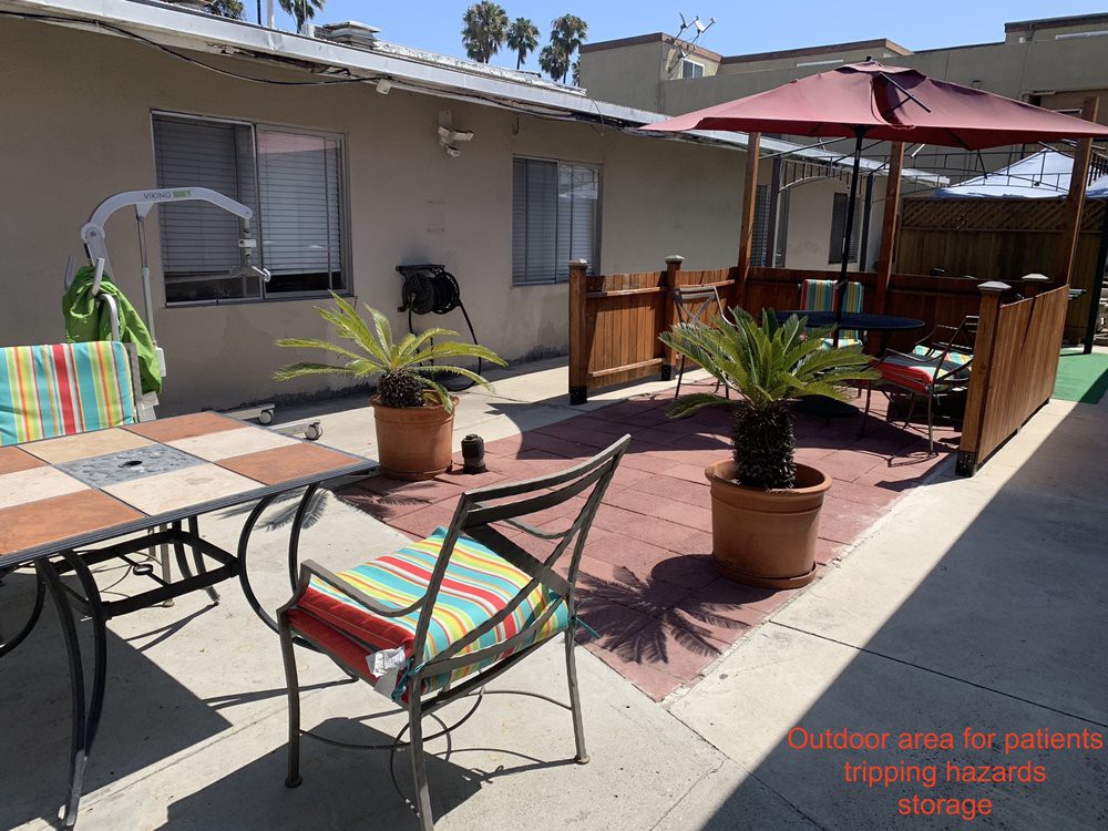 A sunny residential patio with chairs, potted plants, and a large umbrella.